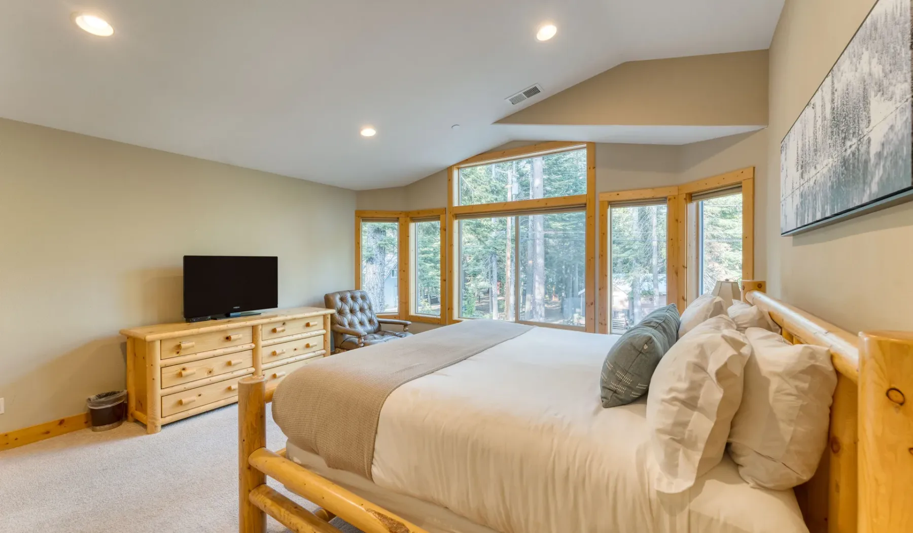 A bedroom with a wooden bed, pale bedding, and large windows.