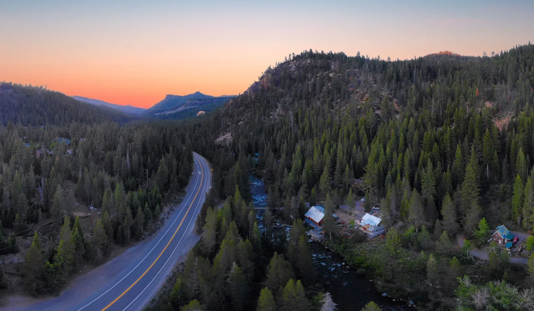 A winding road passes through a forested mountain valley at sunset.