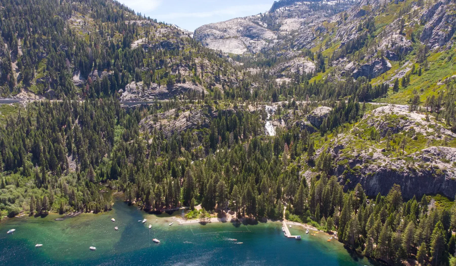 A forested mountain valley rises above a turquoise lake.