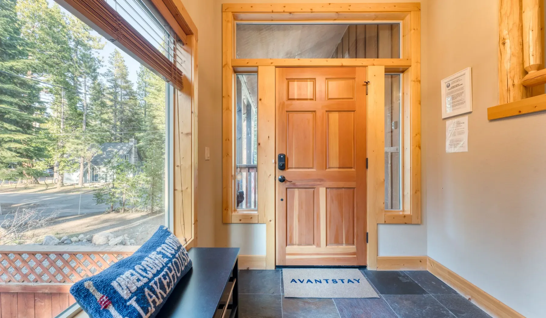 An entryway with a wooden front door and a large window overlooking trees.