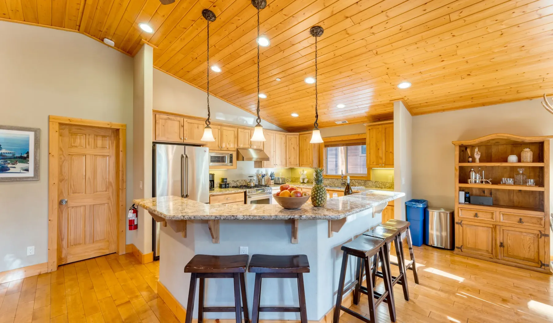 A kitchen with a central island, pendant lights, and wooden cabinetry.