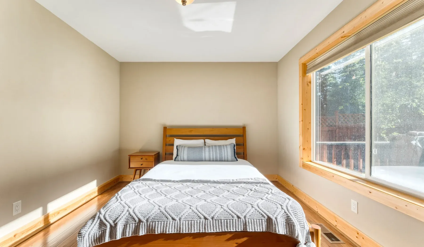 A bedroom with a bed beneath a large sunlit window.
