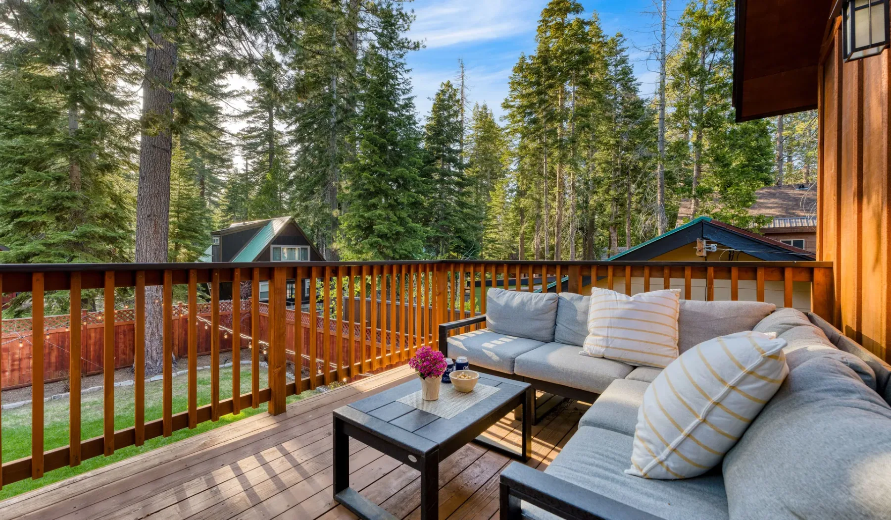 A wooden deck with cushioned seating and a view of evergreen trees.