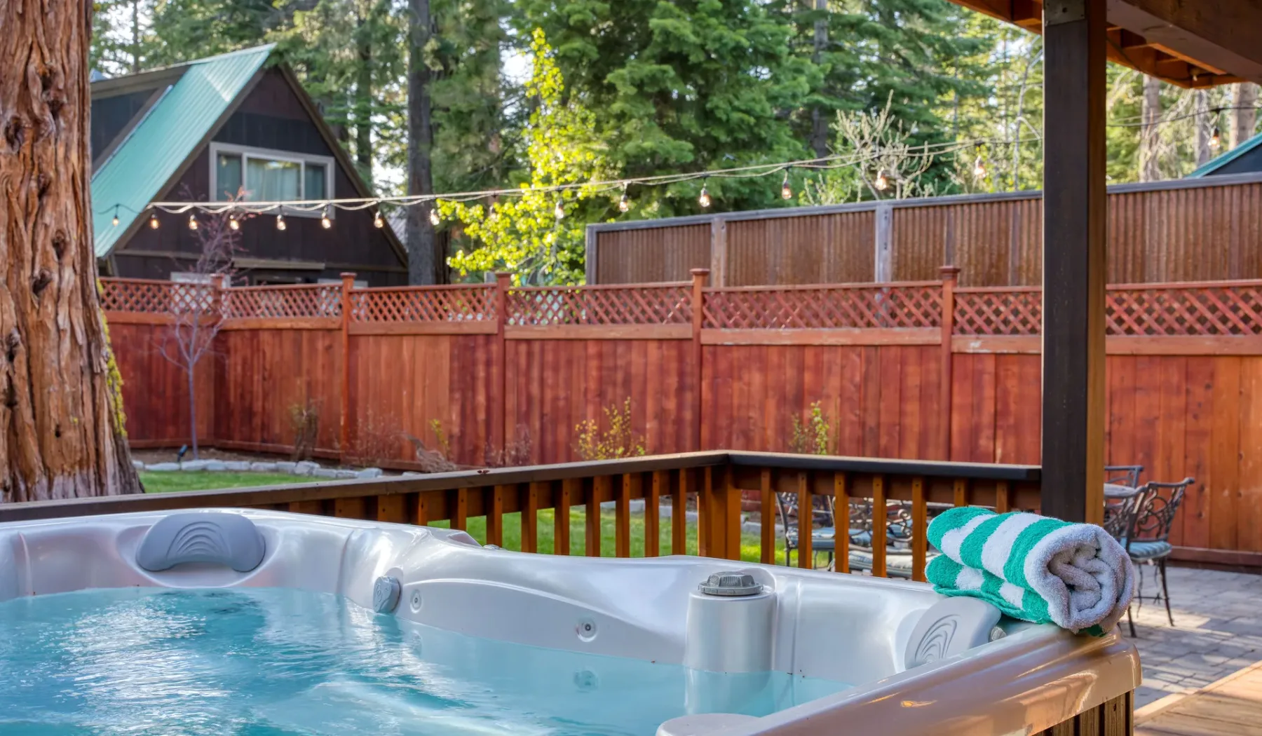 An outdoor hot tub sits on a wooden deck beside a fenced yard.