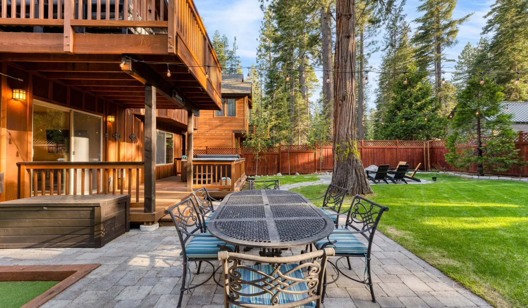 Outdoor patio with a dining table beside a lawn and wooded yard.