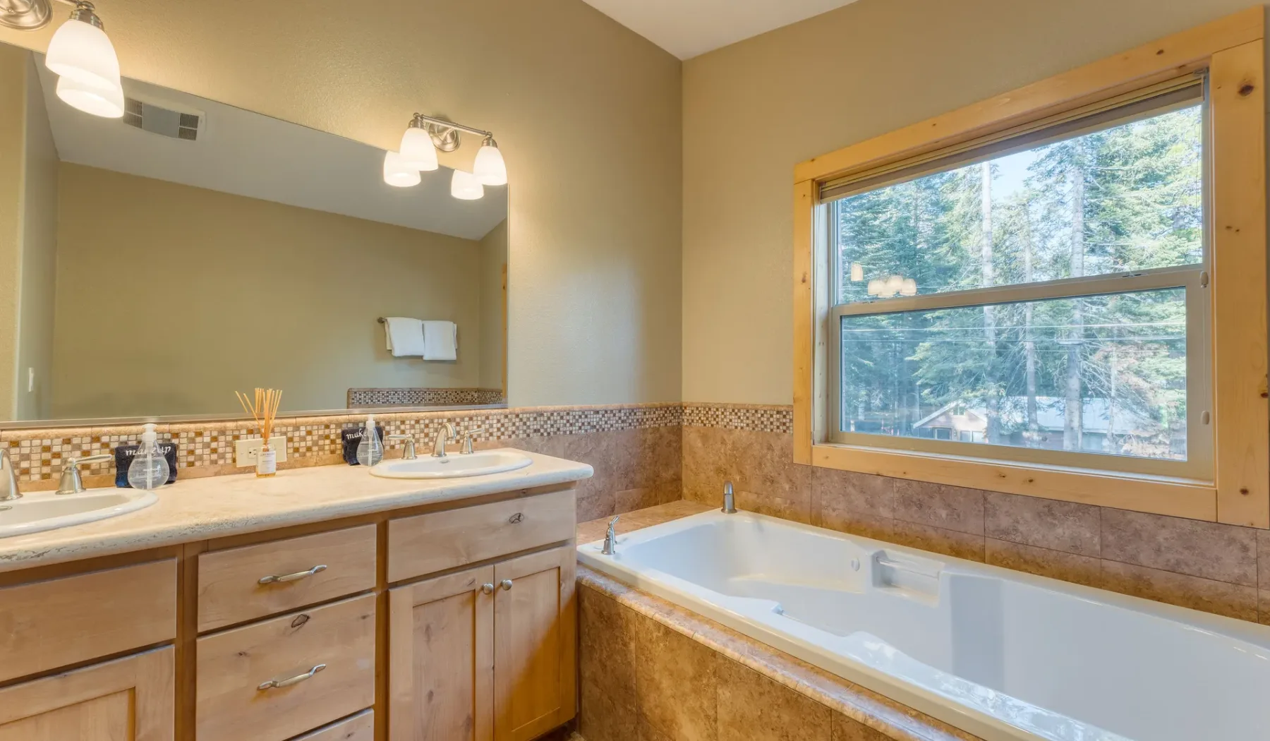 A bathroom with a vanity, wide mirror, and bathtub beside a large window.