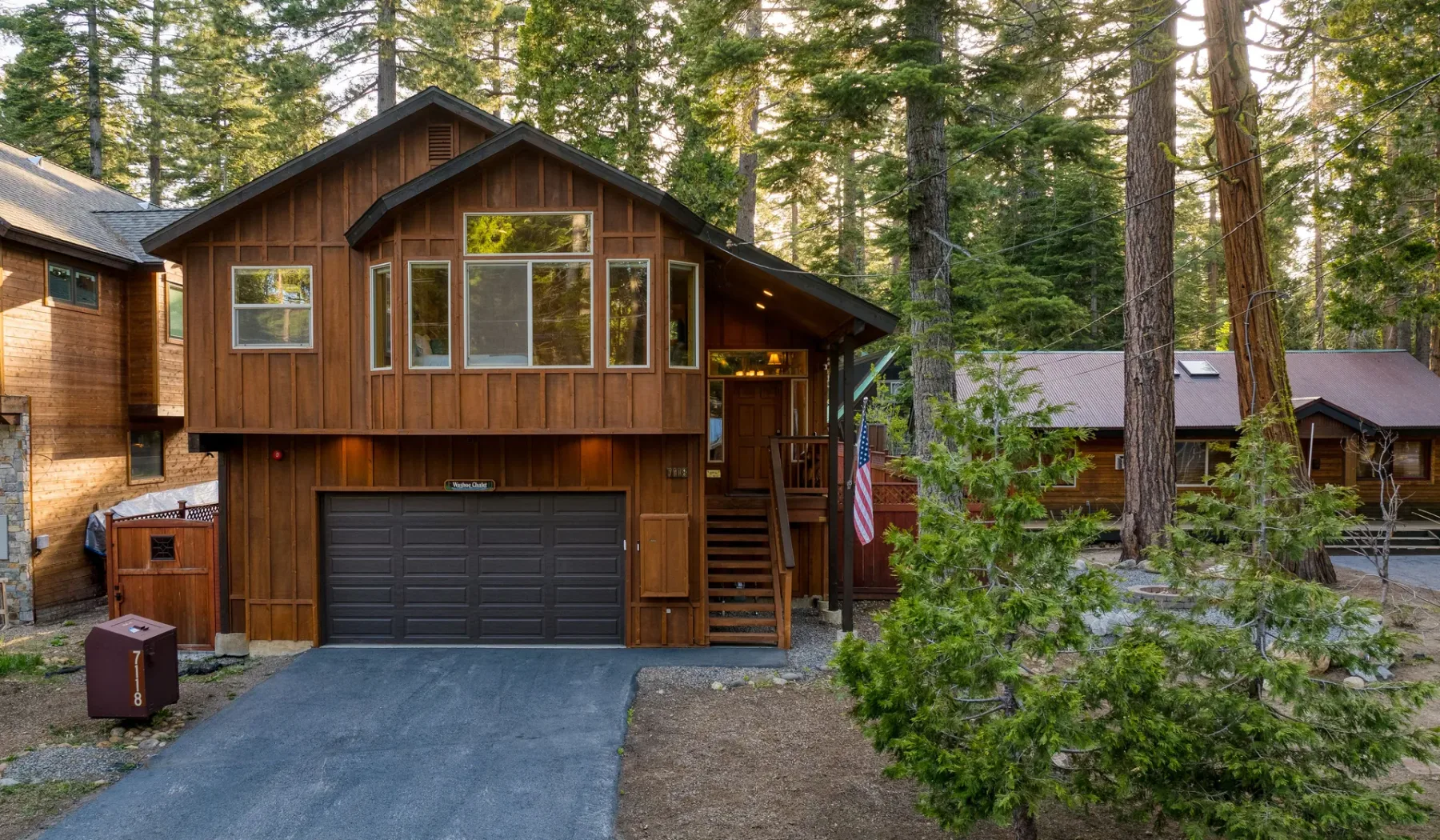 A brown wooden house with an attached garage sits among tall trees.