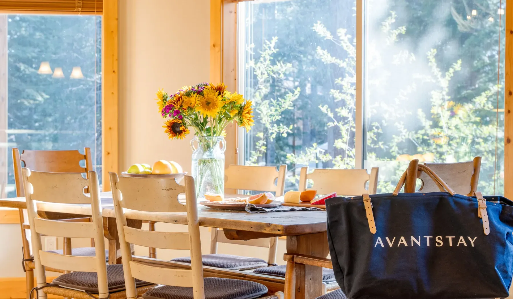 A dining table with chairs and flowers sits beside large windows.