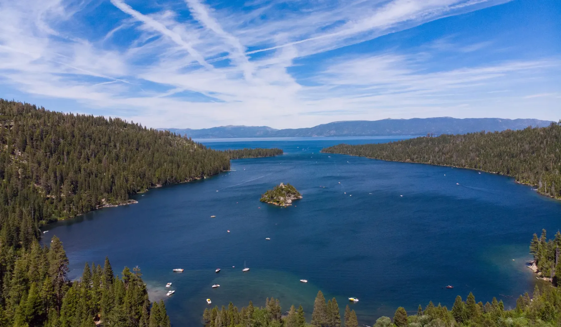 Aerial view of a blue lake surrounded by forested hills beneath a cloudy sky.