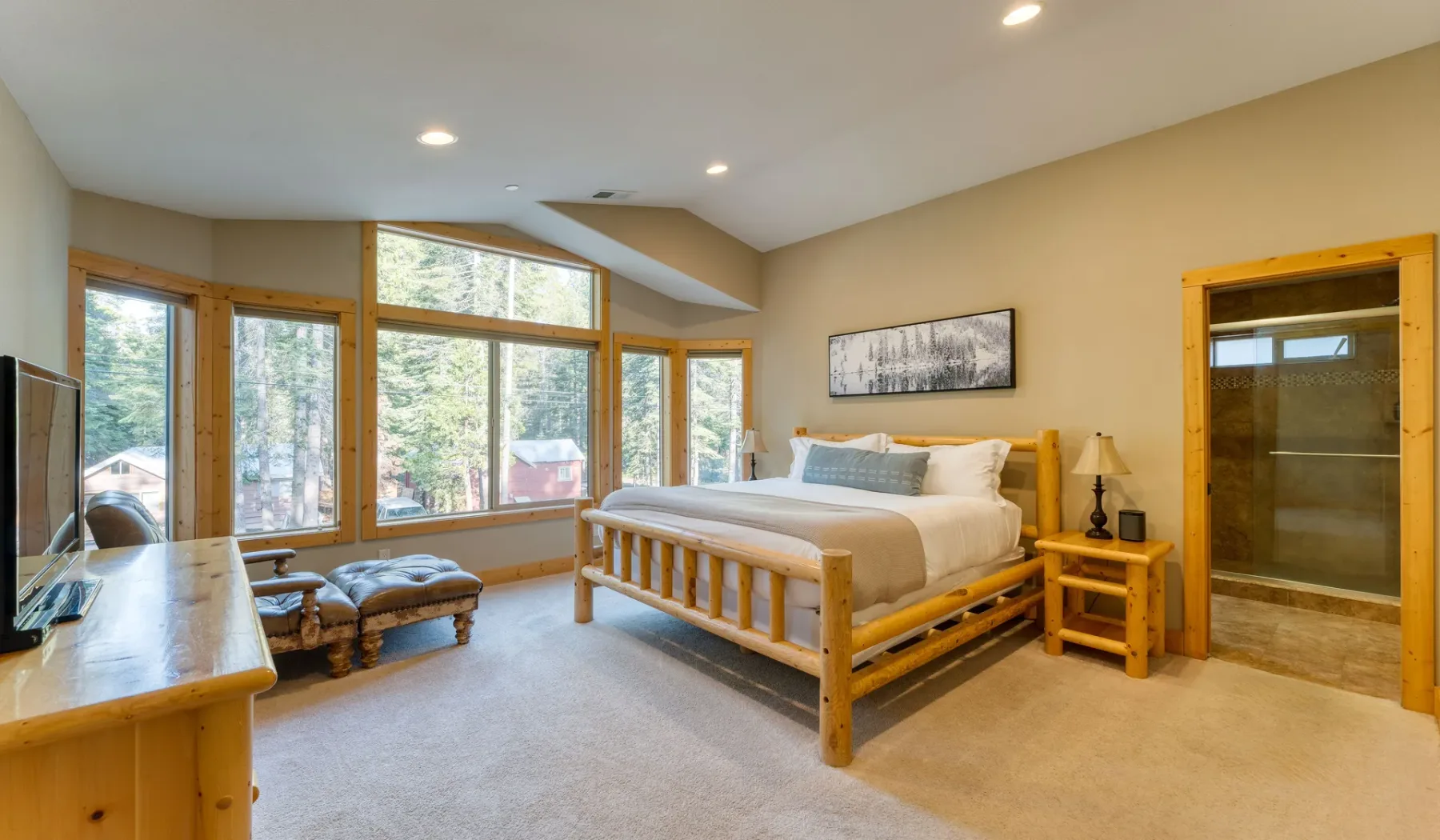 A bright bedroom has a wooden bed, large windows, and a glass shower.
