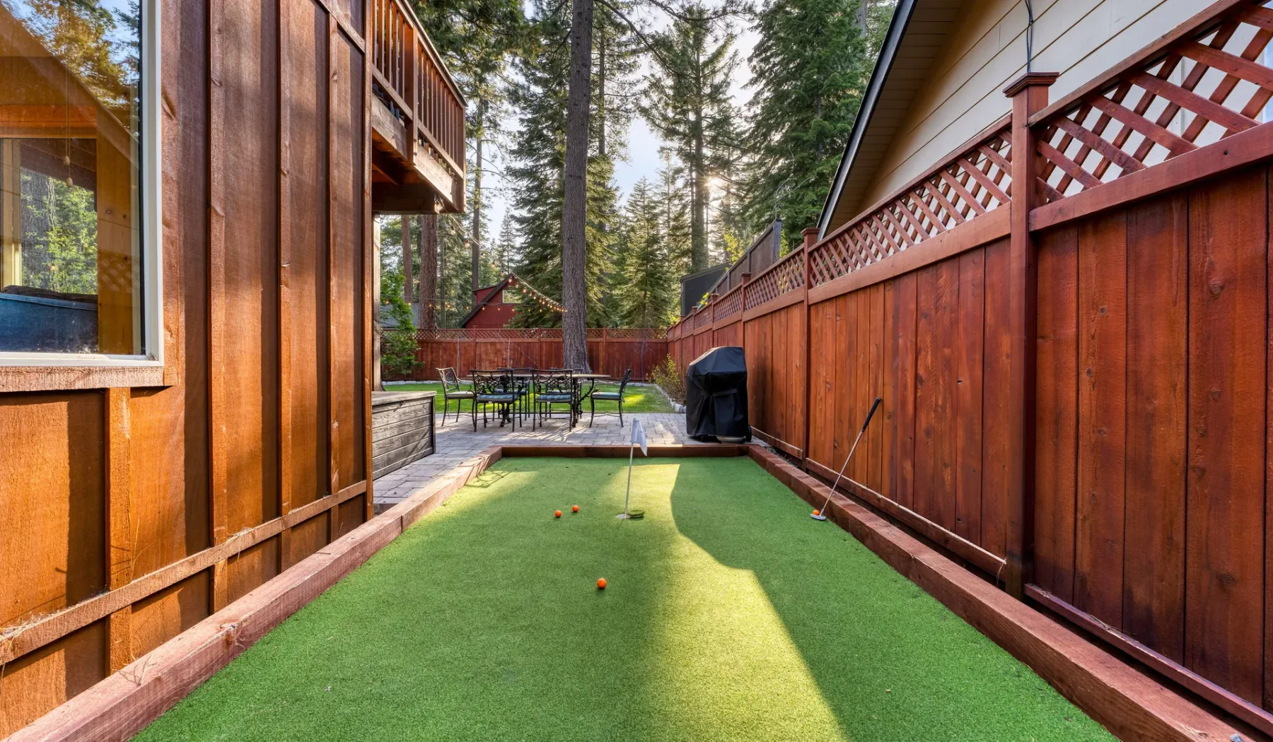 An outdoor putting green sits between wooden fences, with seating at the far end.