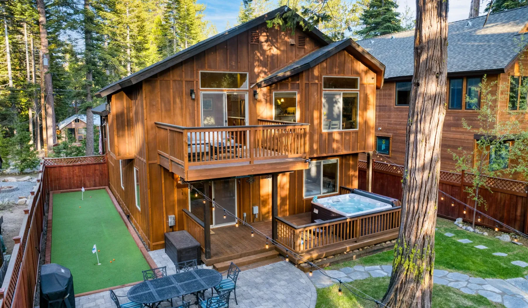 A large wooden house with a raised deck, hot tub, and green game court.