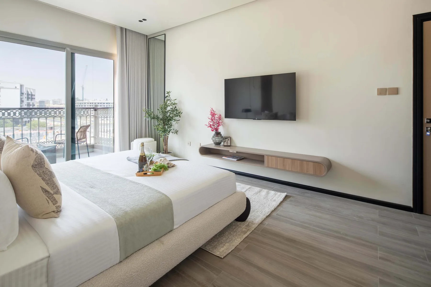 A bedroom with a neatly made bed, wall-mounted television, and sliding glass doors.