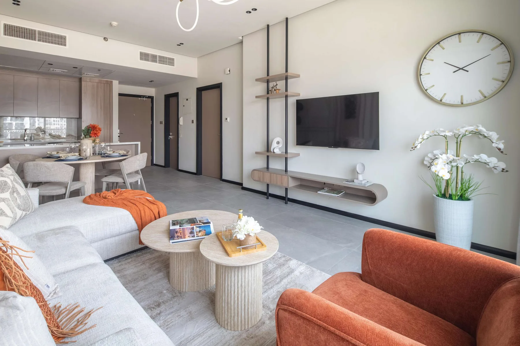 A bright living room with seating, a wall-mounted television, and an open dining area.