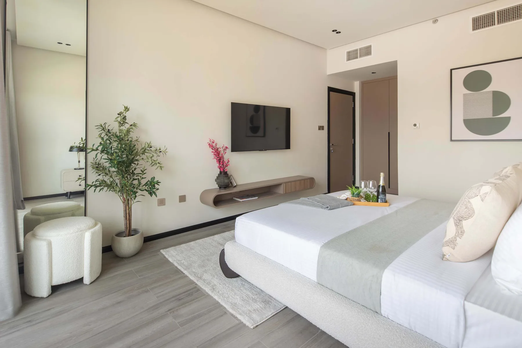 A bright bedroom with a bed, wall-mounted television, and potted plant.
