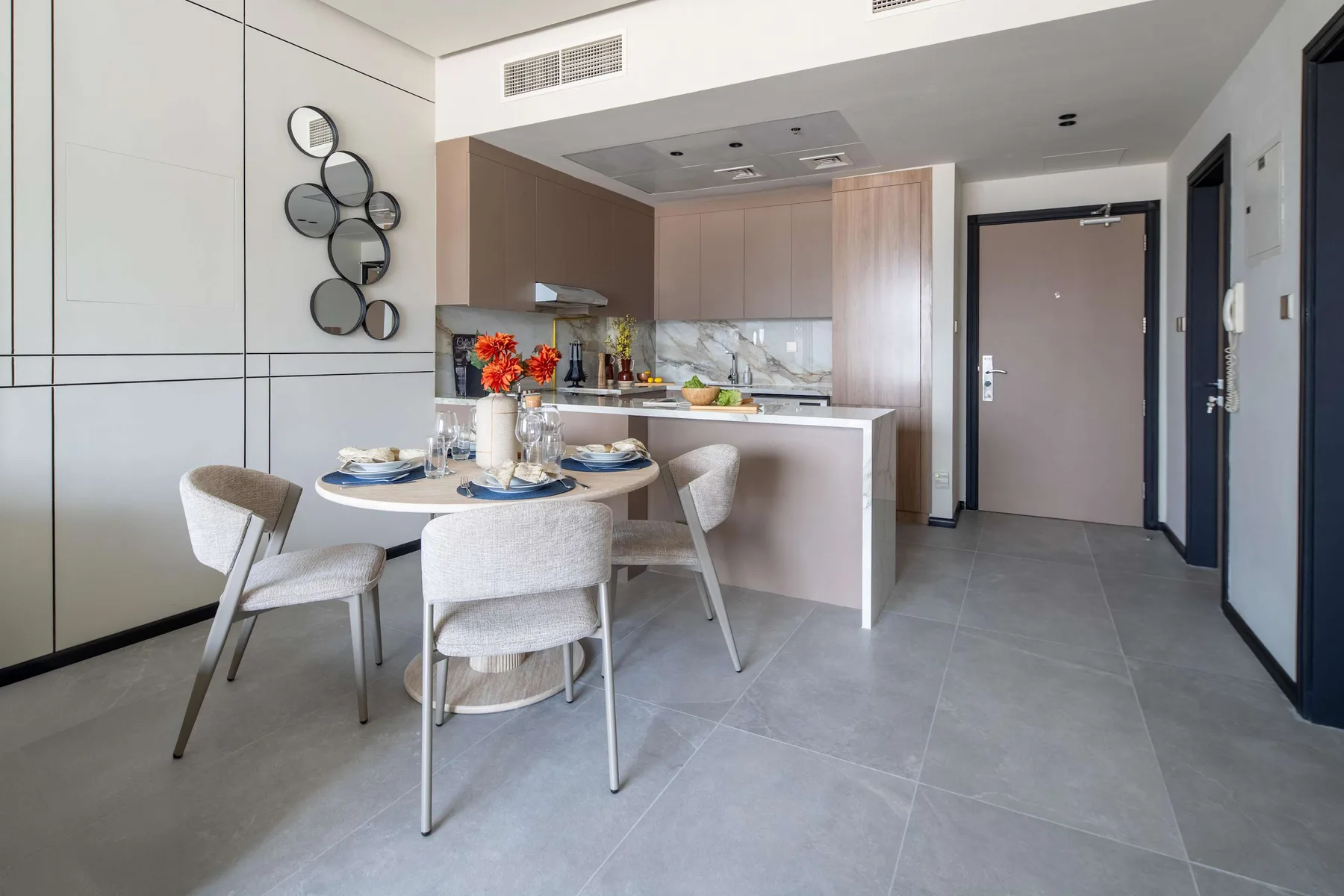 A dining area beside a compact kitchen, with a set table and wall mirror.