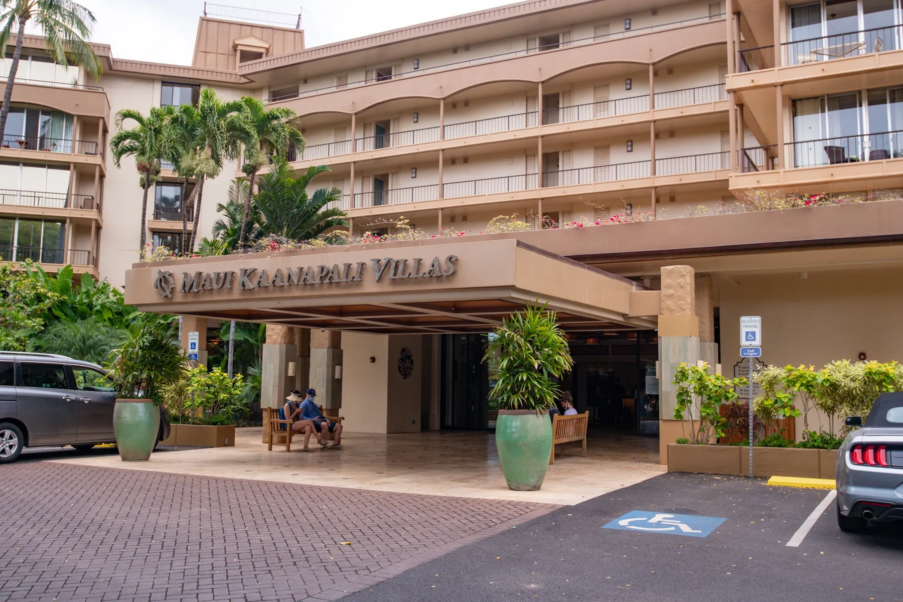 Entrada de hotel bajo una marquesina, con balcones y plantas tropicales.