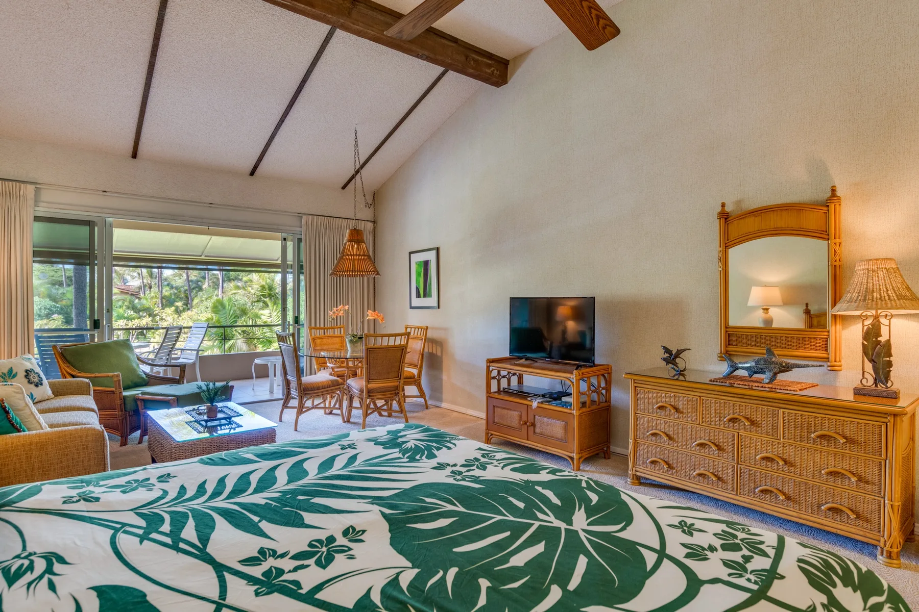 Un dormitorio con una colcha estampada, una zona de estar y una mesa de comedor junto a las ventanas.