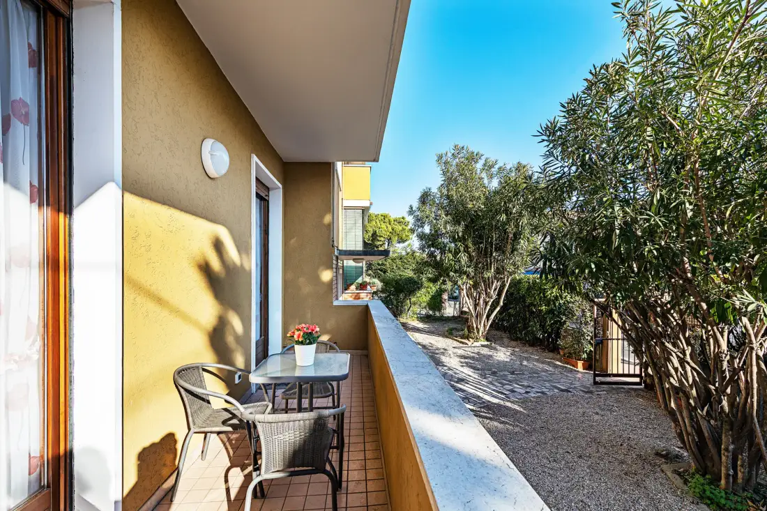 Un pequeño balcón con una mesa y asientos da a un patio arbolado.