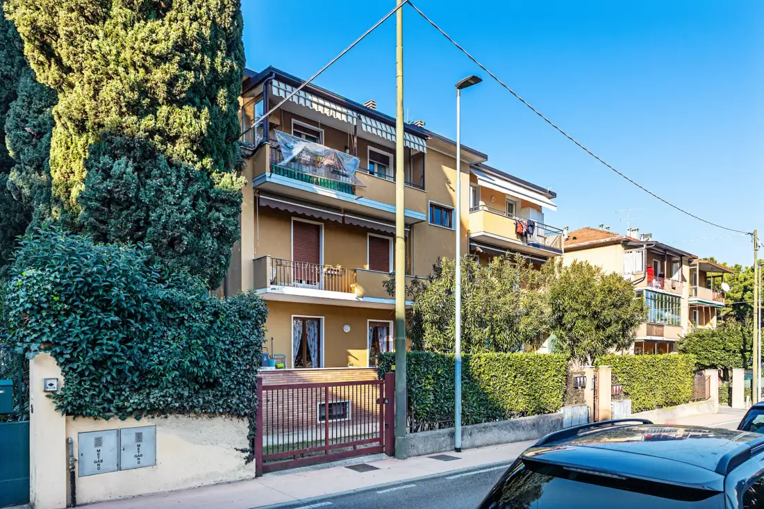 Una calle residencial con casas de varias plantas, setos y coches aparcados.