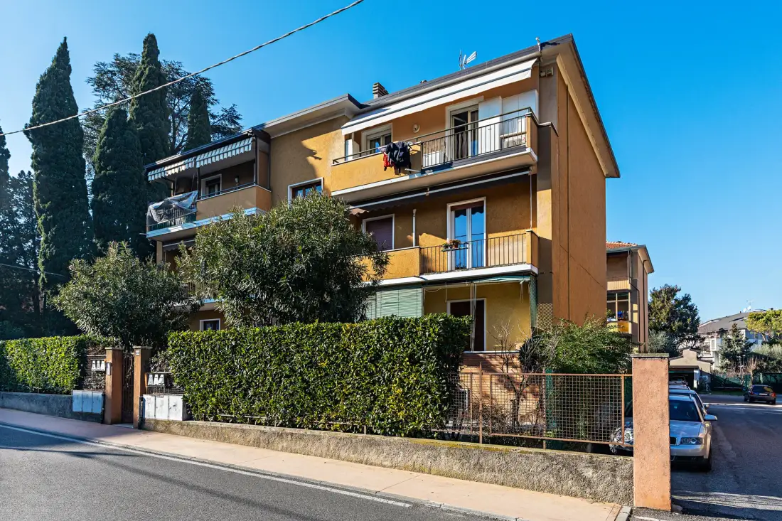 Un edificio residencial de varias plantas se alza tras un seto junto a la calle.