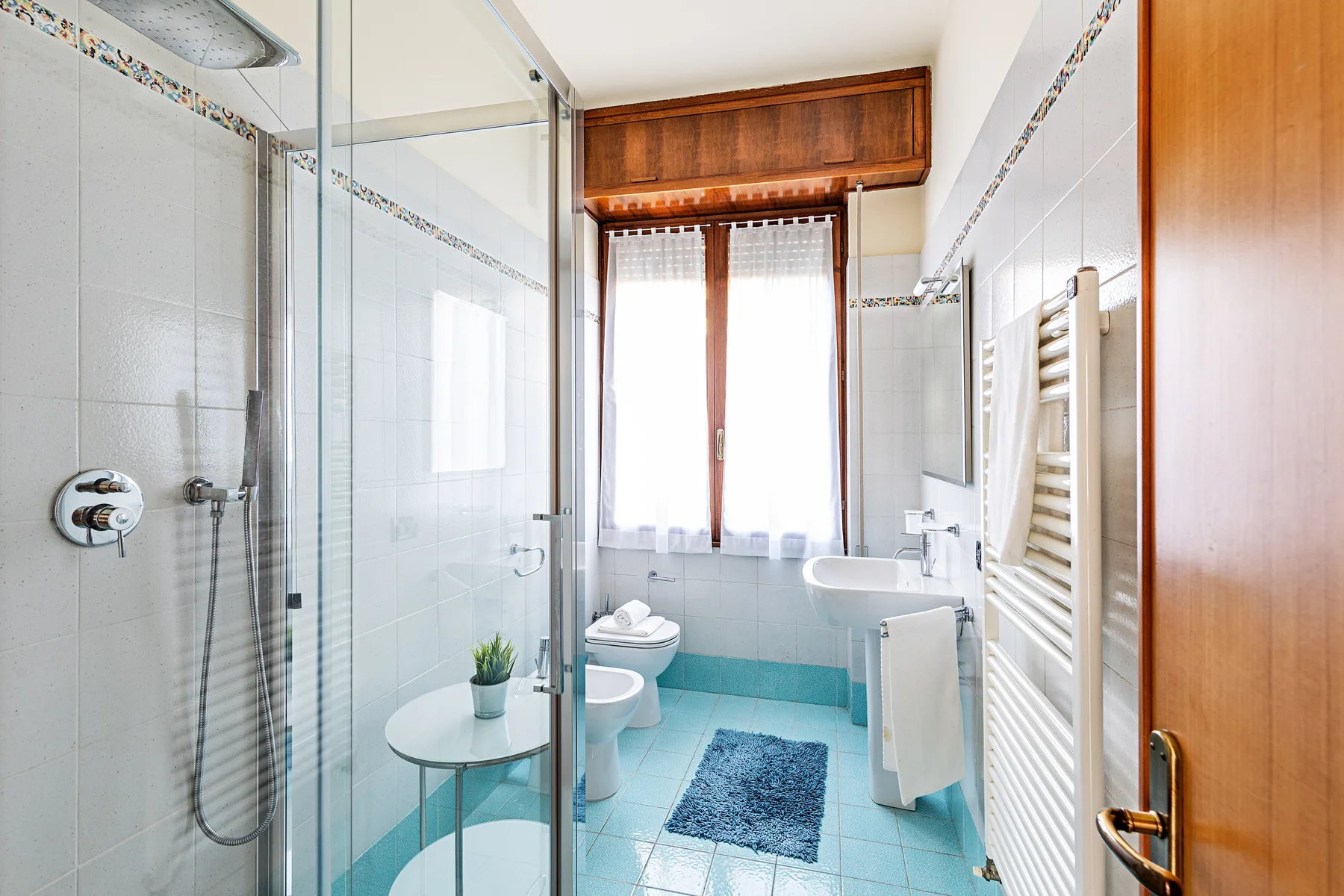 Un baño luminoso con una ducha de vidrio y una ventana sobre el lavabo.