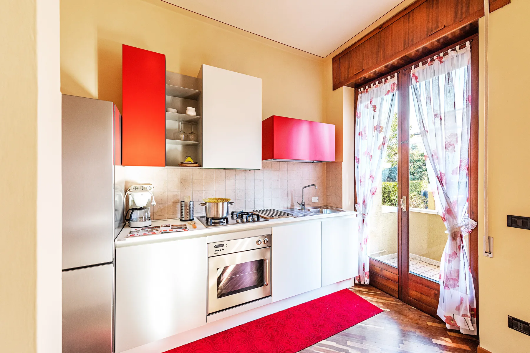 Una cocina luminosa con gabinetes blancos y una alfombra roja.