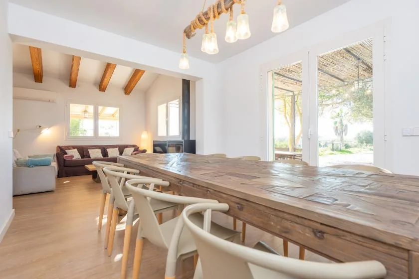 Un comedor luminoso con una larga mesa de madera y asientos junto a grandes ventanales.