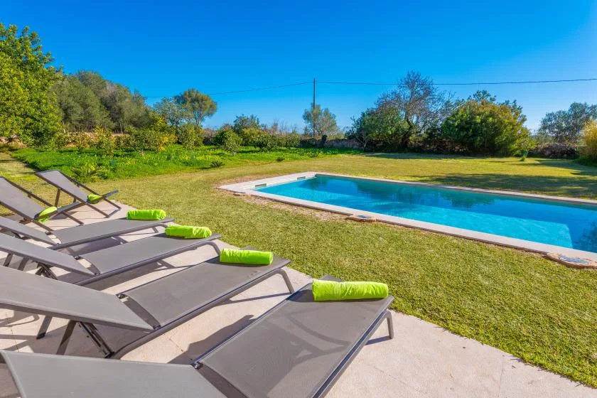 An outdoor swimming pool beside a grassy yard and lounge seating.