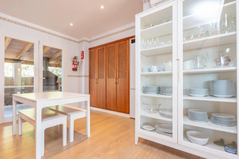 Un comedor con una mesa blanca junto a un armario de vajilla con puertas de vidrio.
