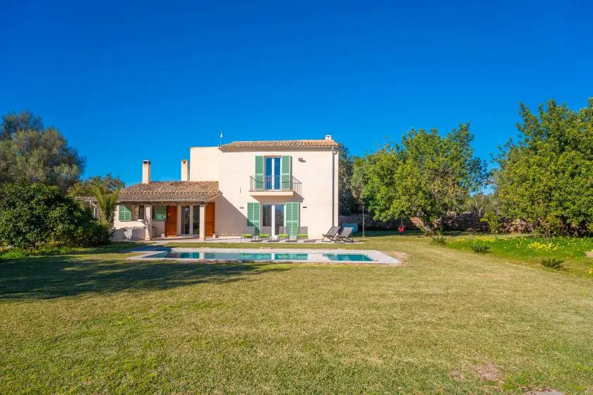 Una casa de dos plantas está junto a una piscina en un amplio jardín con césped.