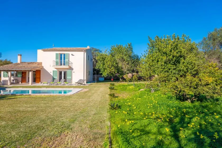 Una casa y una piscina dan a un césped soleado y un jardín.