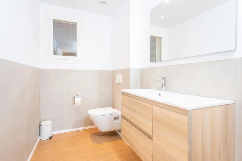 Un baño luminoso con un inodoro y un mueble de lavabo en tono madera.
