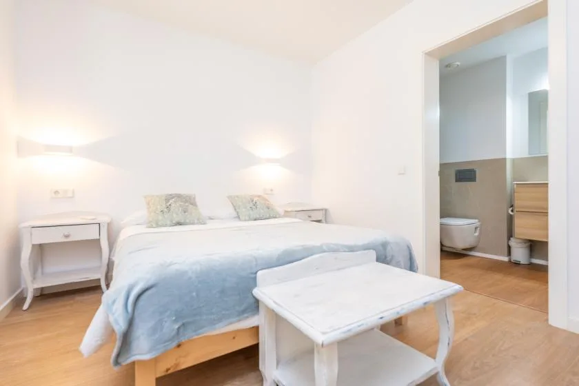 Un dormitorio luminoso con una cama, mesas de noche y una puerta abierta al baño.