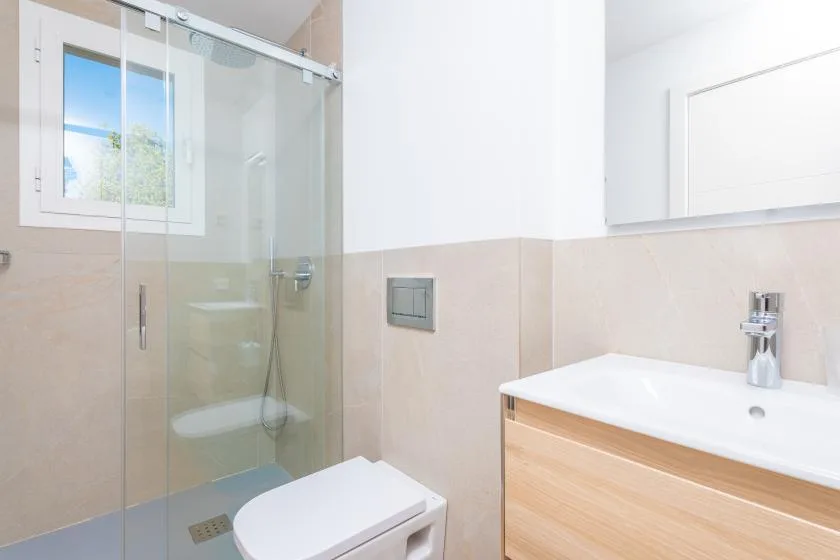 Un baño luminoso con ducha de cristal, inodoro y lavabo con mueble.