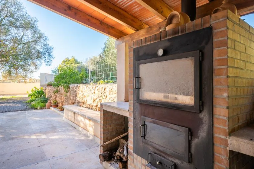 Una zona de cocina exterior cubierta con un gran horno de ladrillo junto a un patio pavimentado.