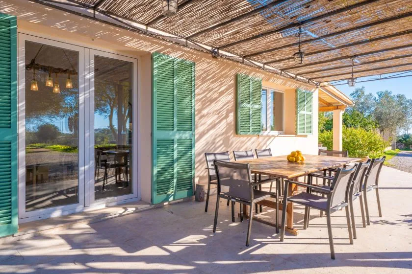 A shaded outdoor dining area with a table and chairs beside a house.