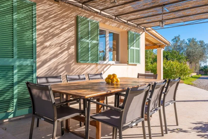 Una zona de comedor exterior a la sombra, con una mesa larga y sillas.