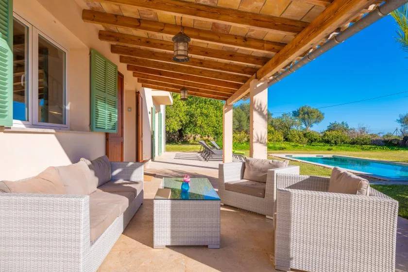 Una zona de estar exterior cubierta da a un jardín y una piscina.