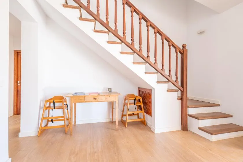 Un pasillo interior luminoso con una escalera de madera y un pequeño escritorio debajo.