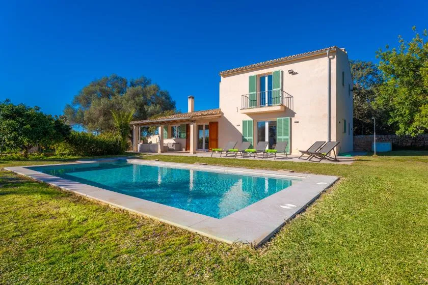 Una casa y una piscina se encuentran en un jardín soleado.
