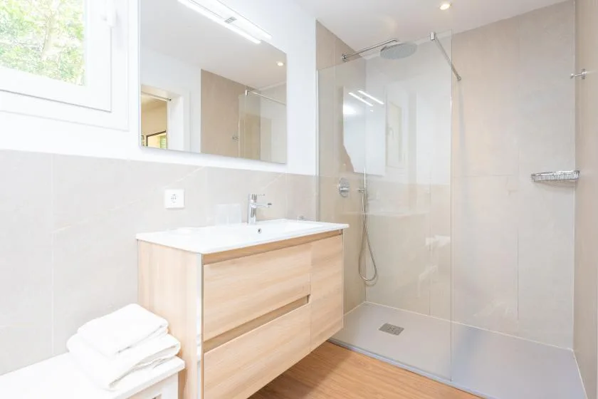 Un baño luminoso con un mueble de madera clara y una ducha de vidrio.