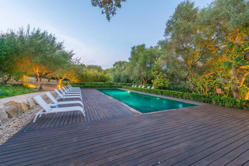 Una piscina al aire libre junto a una terraza de madera y asientos de descanso.