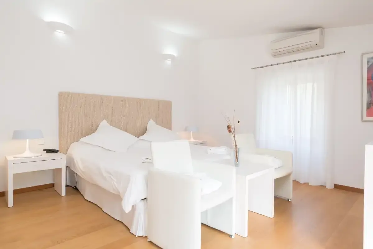 Un dormitorio luminoso con una cama, asientos blancos y una mesita de noche.