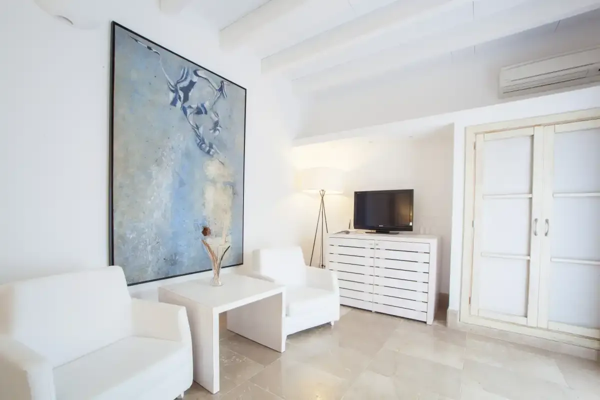 Una sala luminosa con asientos blancos, un televisor y un gran cuadro abstracto.