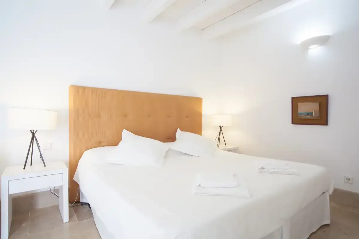 Un dormitorio luminoso con una cama, ropa de cama blanca y un cabecero de madera.