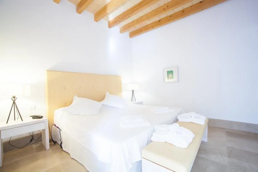 Un dormitorio luminoso con una cama blanca y un cabecero tapizado claro.