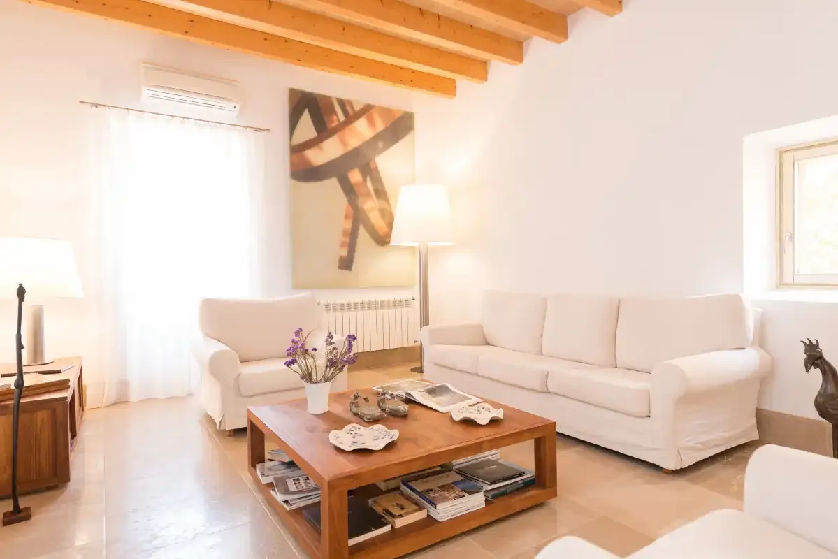 Una sala luminosa con sofás, una mesa de centro de madera y vigas expuestas en el techo.