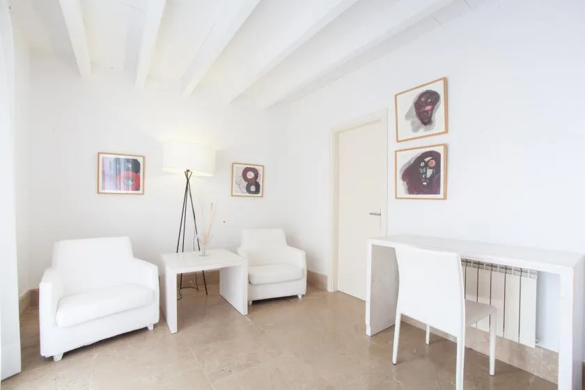 Una luminosa zona de estar con asientos blancos, cuadros y una mesa pequeña.