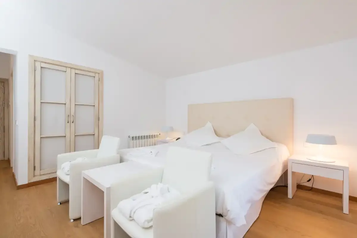 Un dormitorio luminoso con una cama grande y asientos blancos.